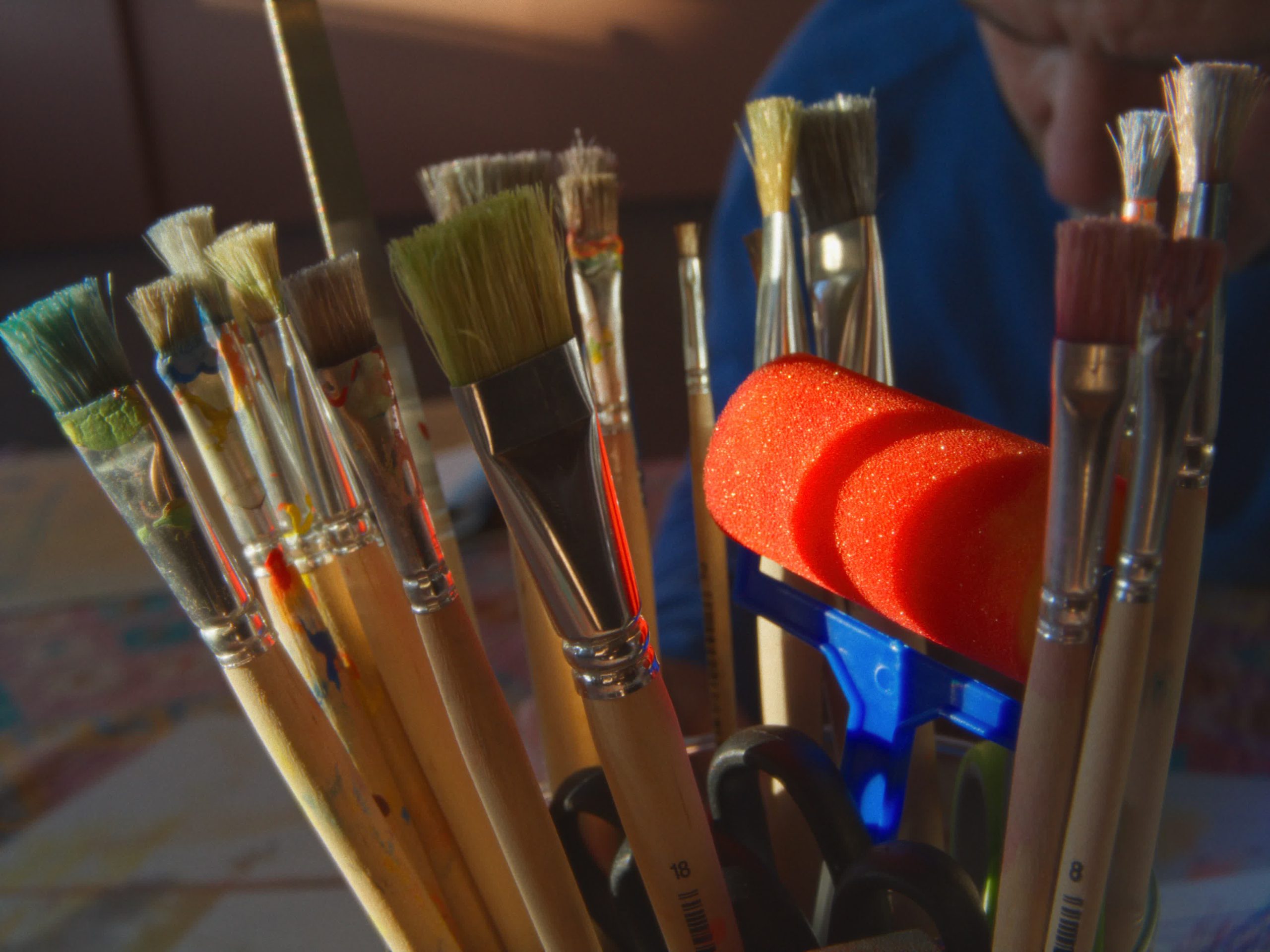 Eine Makroaufnahme eines Behälters voller verschiedener Pinsel und Malutensilien, mit bunten Schwämmen und Rollen im Hintergrund.