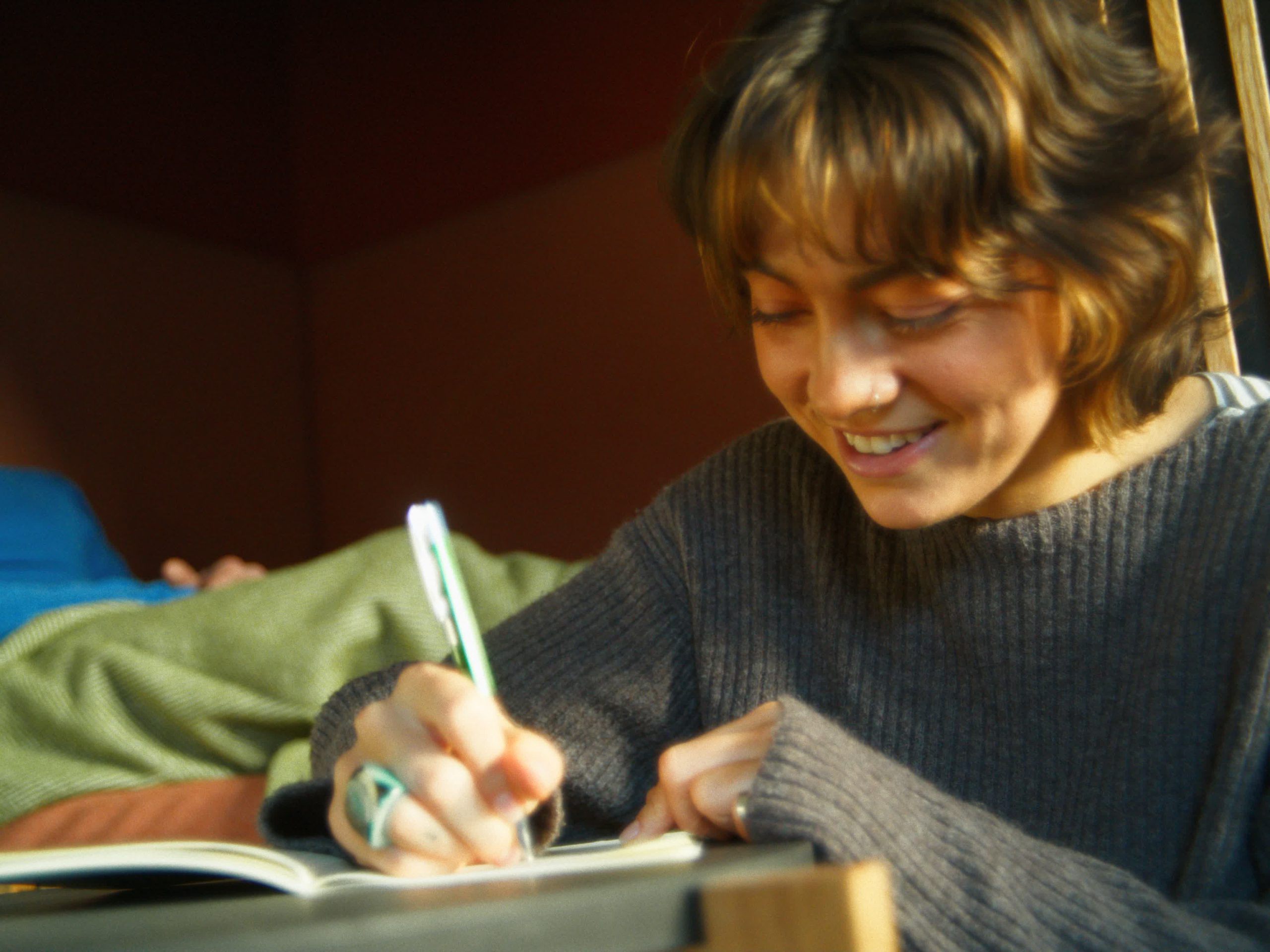 Eine Nahaufnahme einer lächelnden Person, die konzentriert mit einem Stift in ein Tagebuch schreibt – ein Moment der persönlichen Reflexion.