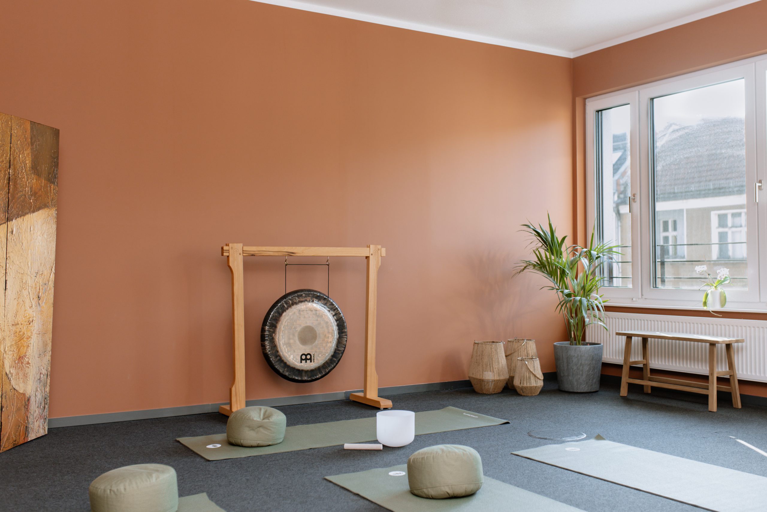 Ein friedlicher, leerer Meditationsraum mit terracottafarbenen Wänden, ausgestattet mit Yogamatten, Meditationskissen und einem großen Gong.