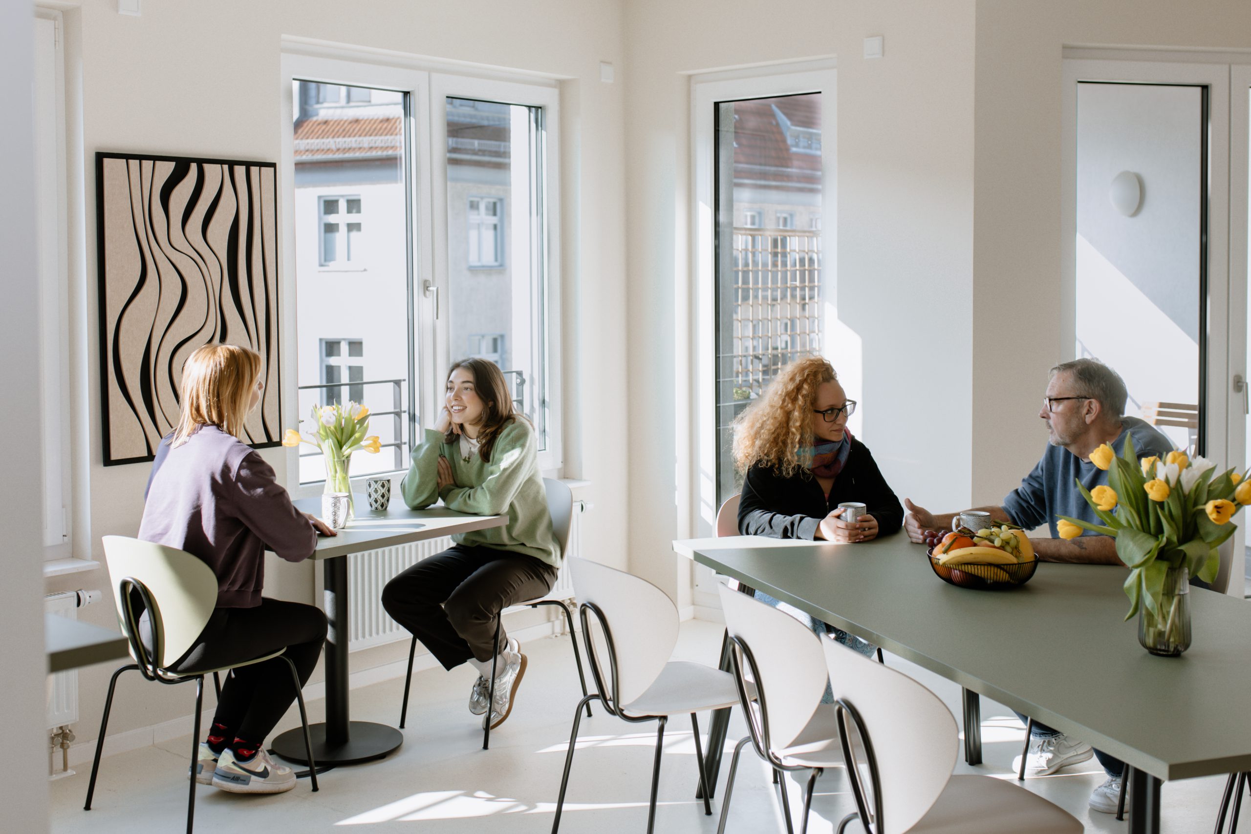 Ein heller, lichtdurchfluteter Raum, in dem Menschen an Tischen sitzen und sich in einer entspannten und freundlichen Atmosphäre unterhalten.