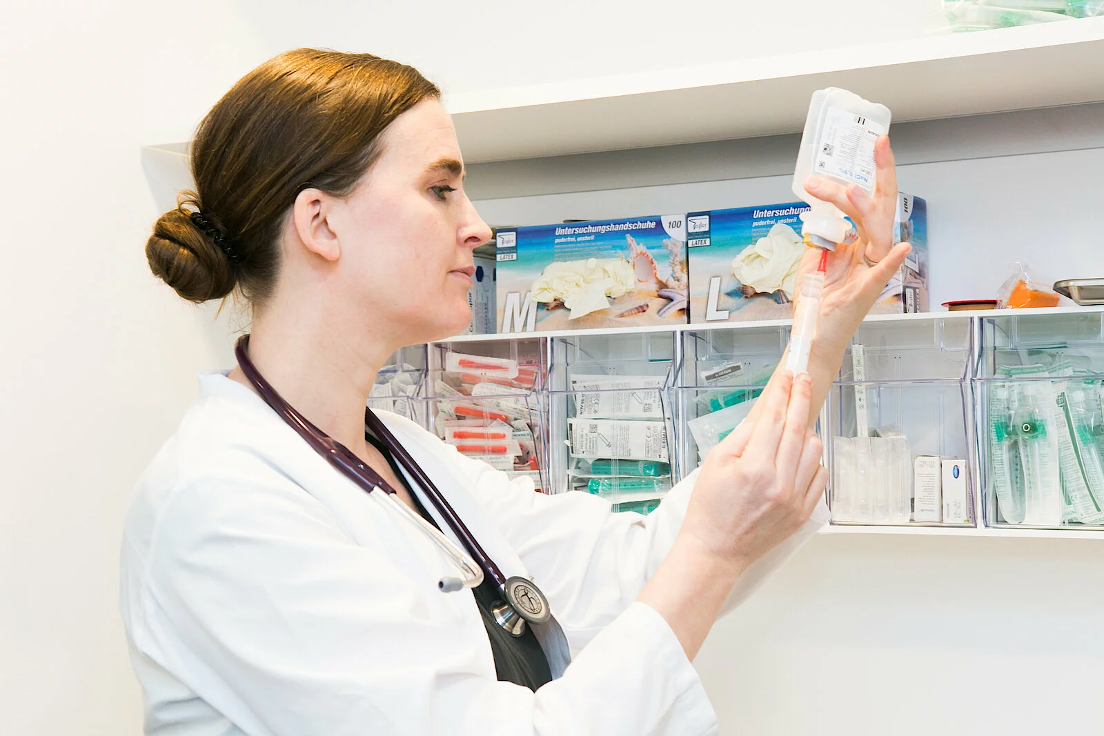 Eine Ärztin im weißen Kittel mit Stethoskop untersucht sorgfältig eine medizinische Ampulle in einer hellen Apotheke oder einem Behandlungsraum.